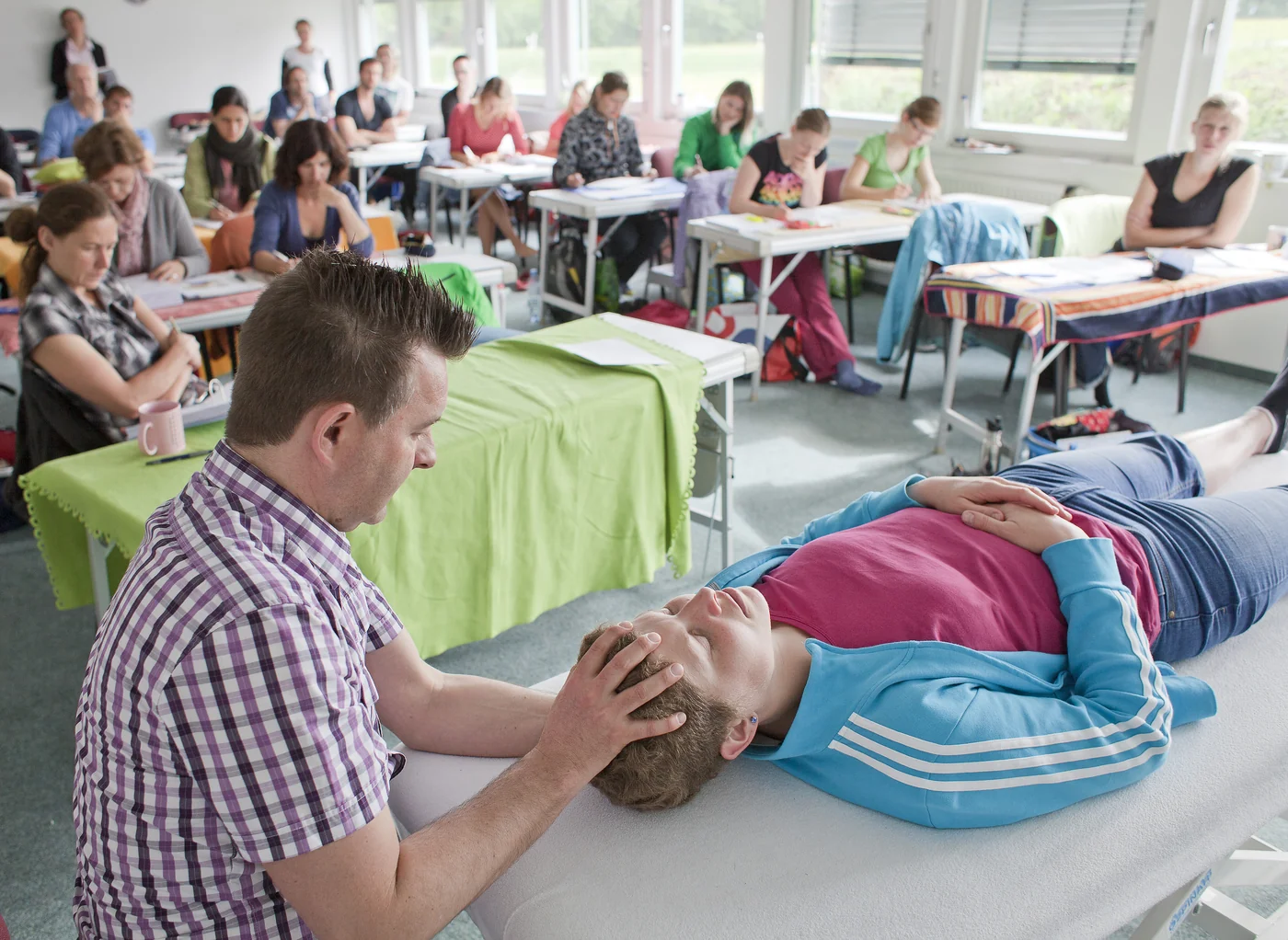 Dozent demonstriert am Kopf eines liegenden Patienten, der Kurs schaut zu